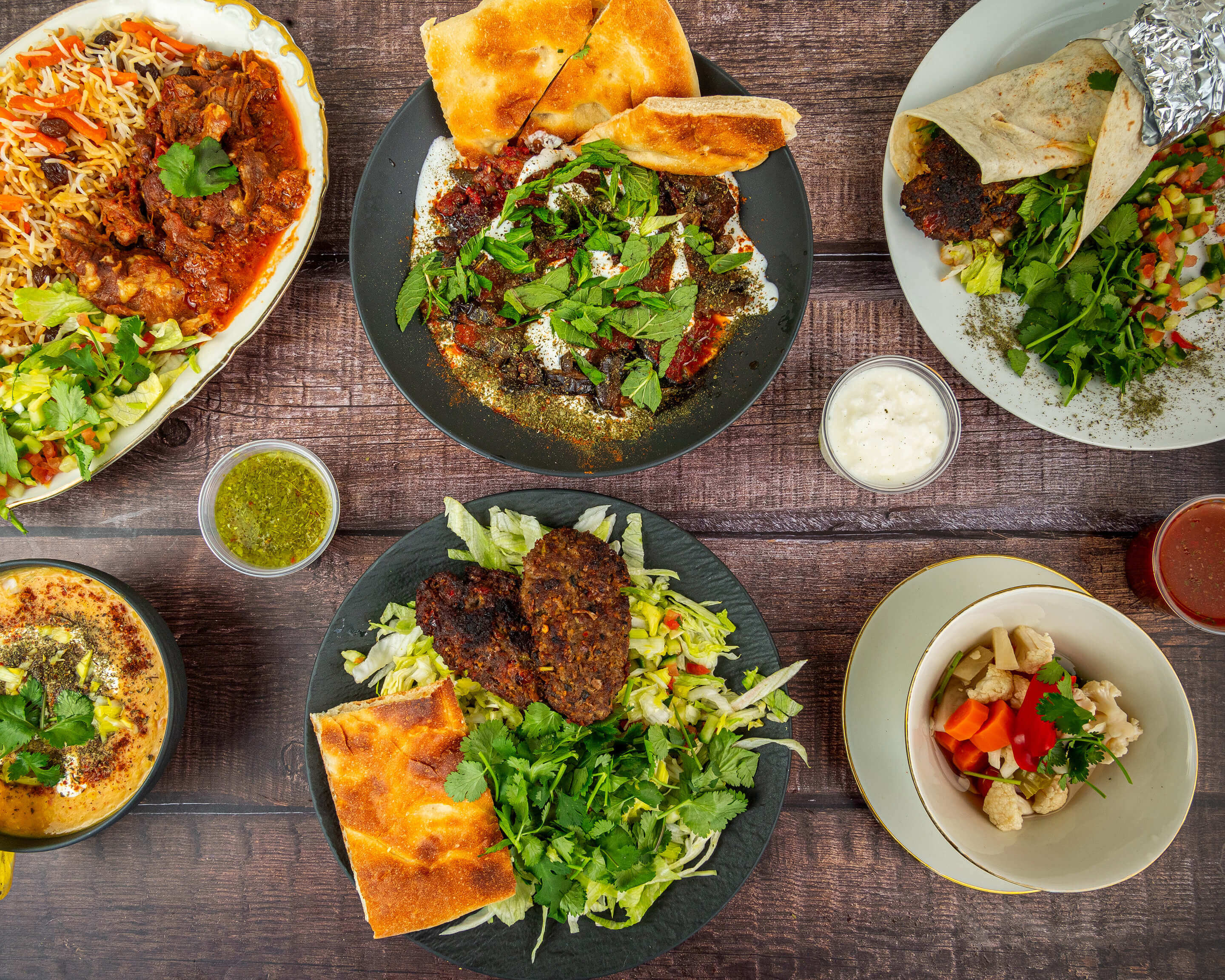 Traditionelle afghanische Gerichte und Dips, kunstvoll angerichtet auf einem rustikalen Holztisch – mit Kräutern, Fladenbrot, Joghurt und Gewürzen. Impression aus dem Afghanischen Kochkurs in Düsseldorf.