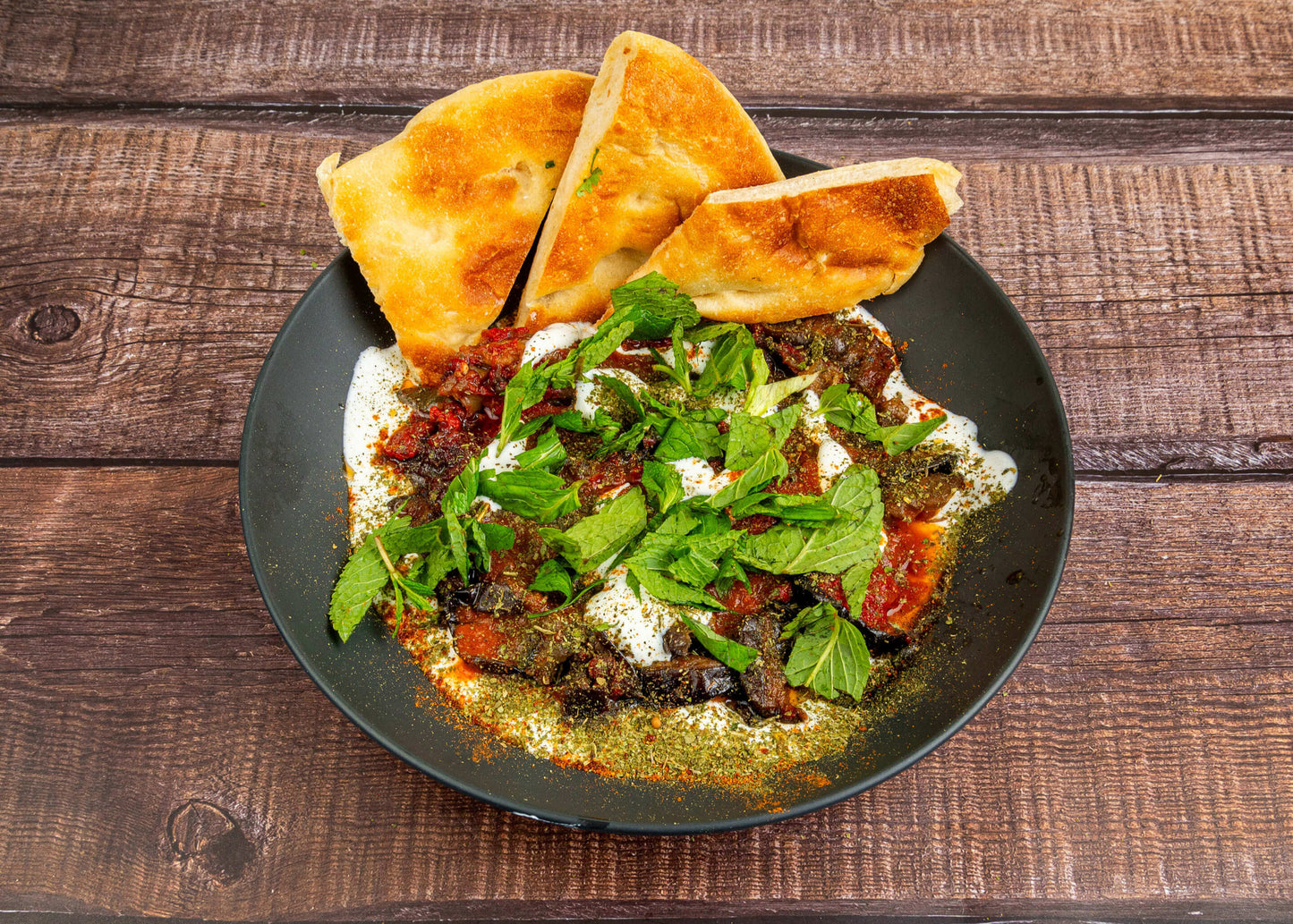 Borani Banjan mit Aubergine, Tomaten und Joghurt, serviert auf schwarzem Teller mit frischer Minze und Fladenbrot – Afghanischer Kochkurs in Düsseldorf